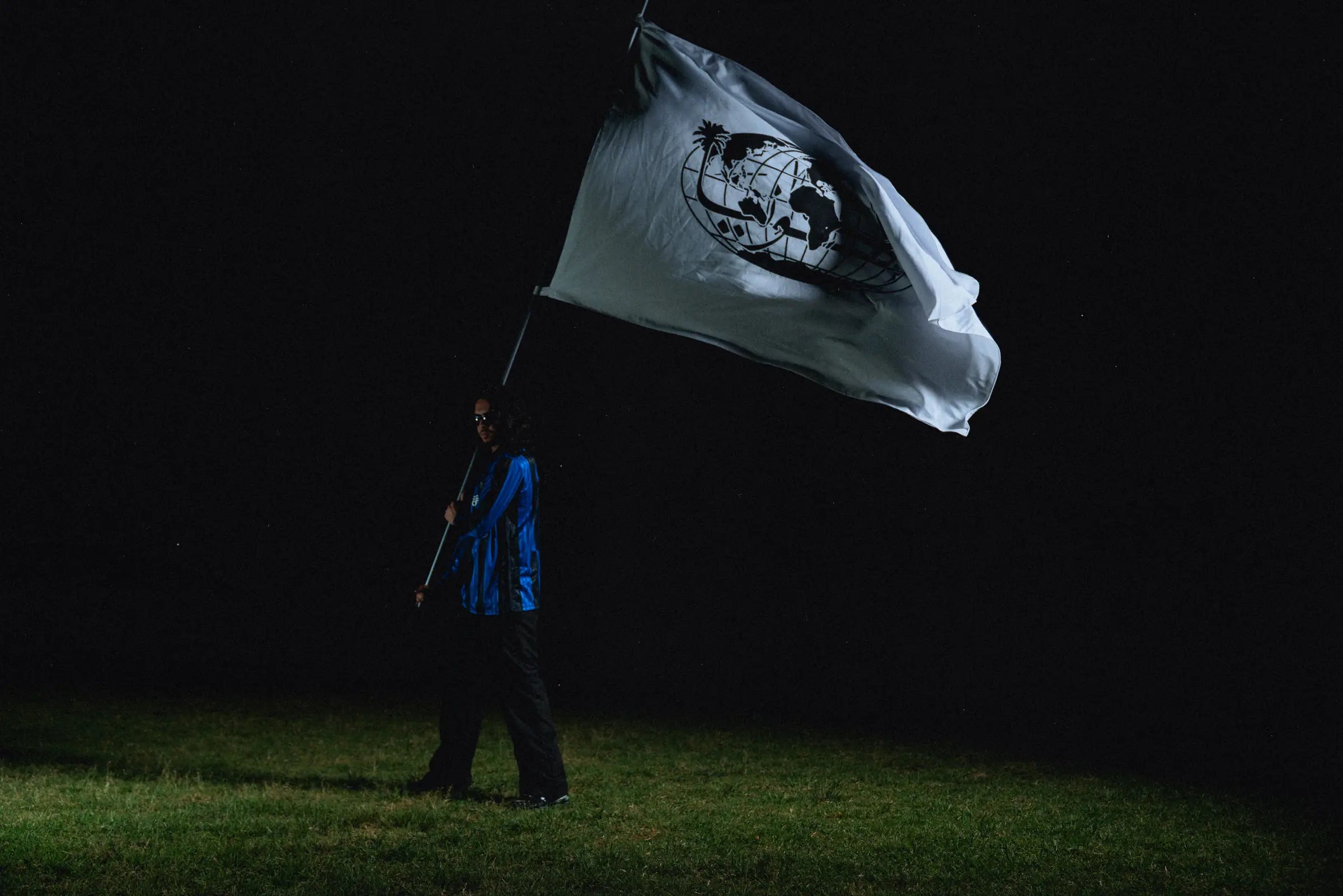At night on a football pitch, a model holds up a large white Morocconia flag printed with the palm-tree globe.